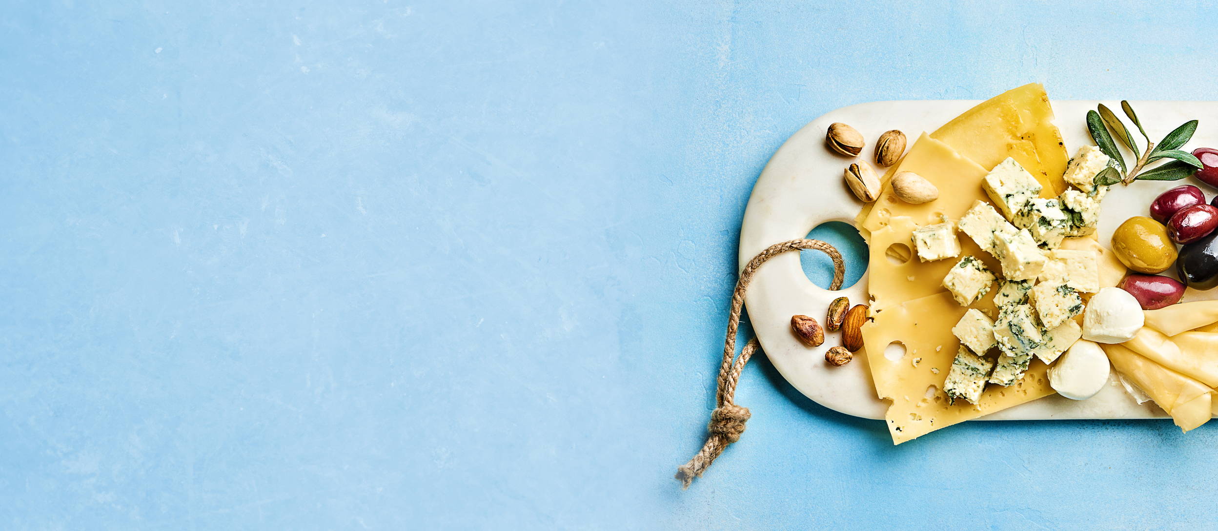 A birds eye view of a white charcuterie board covered in a variety of hard and soft cheeses and fruits for Confetti's Virtual Food Tasting Kits