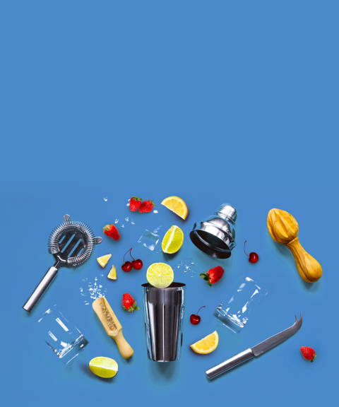 A cocktail shaker surrounded by various fruits, citrus reamers, glasses, ice, and a knife for Confetti's Virtual Holiday Mixology Class