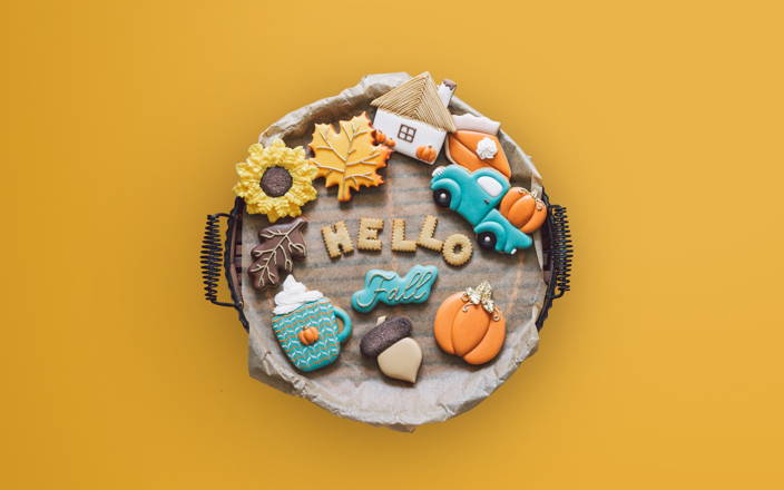 A plate of cookies iced and shaped in various autumnal shapes like pieces of pie, pumpkins, leaves, and more for Confetti's Virtual Fall Cookie Decorating Class
