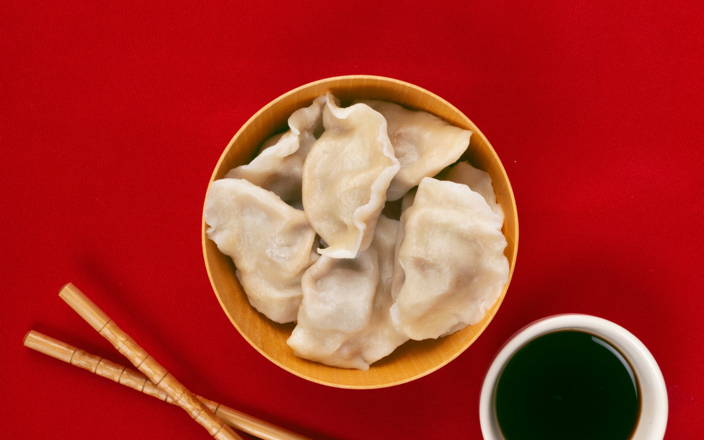 Dumplings in a bowl next to chopsticks and soy sauce for Confetti's Virtual Team Cooking Classes
