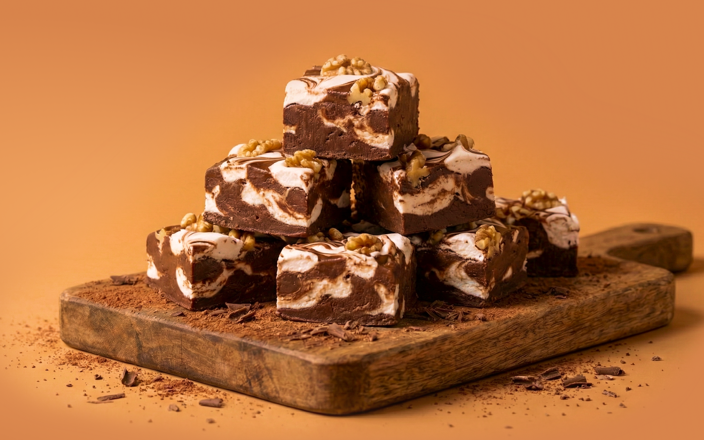 Pieces of fudge stacked on top of each other. Fudge has marshmallow swirls and walnuts.