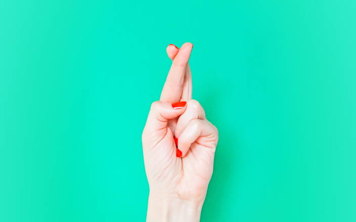 A hand with red nail polish crossing their pointer and middle fingers for Confetti's Virtual Two Truths and a Lie Team Building