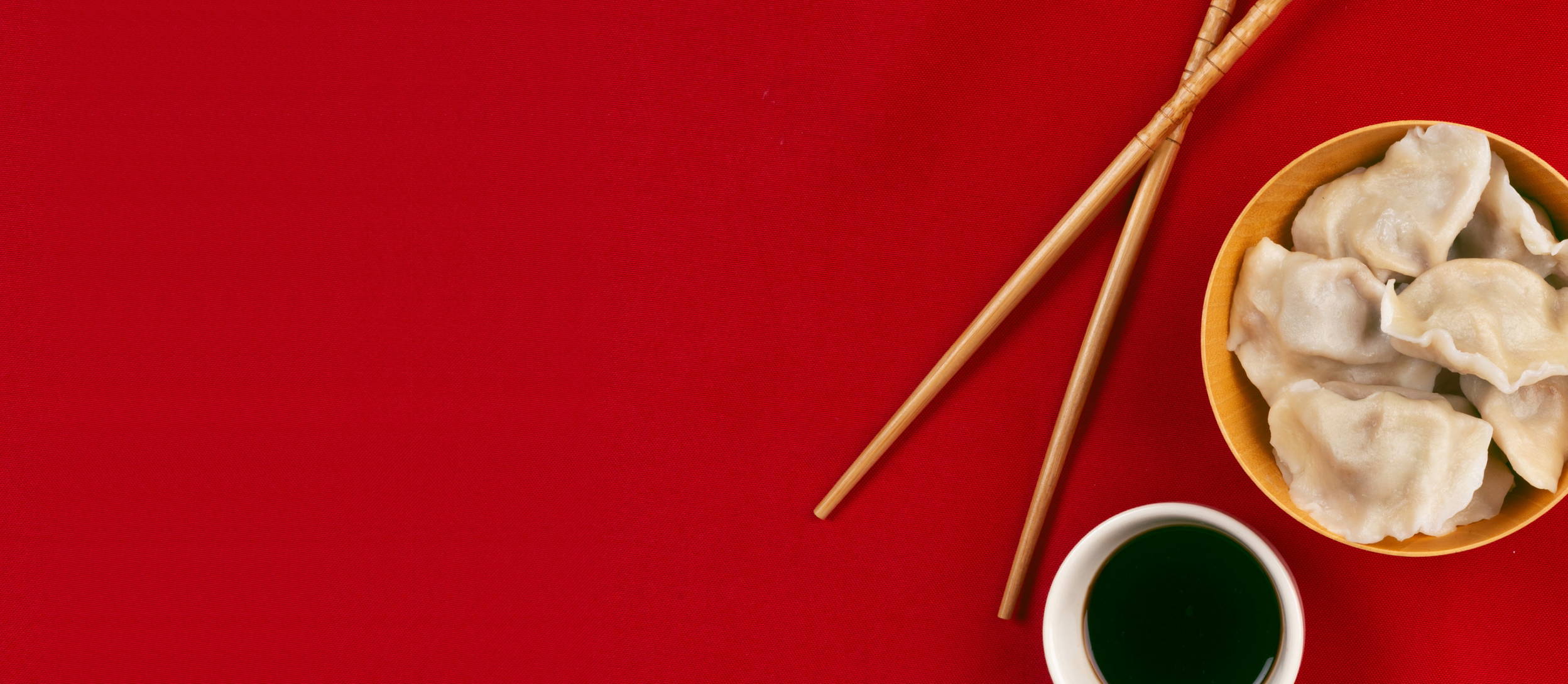 Dumplings in a bowl next to chopsticks and soy sauce for Confetti's Virtual Team Cooking Classes