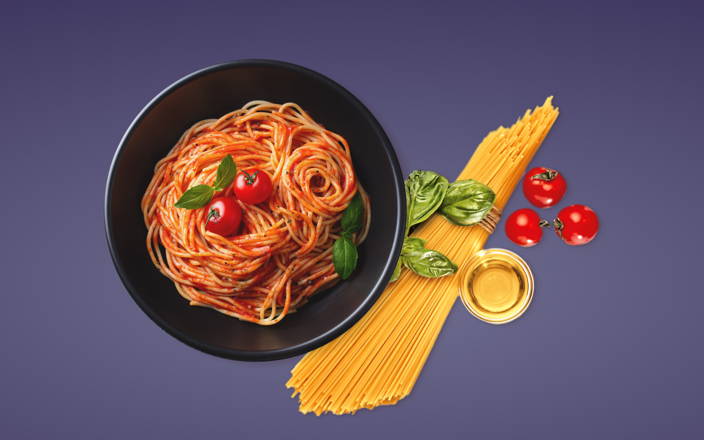 A plate of spaghetti next to a bundle of pasta, basil, and tomatoes for Confetti's Virtual Cooking Workshop