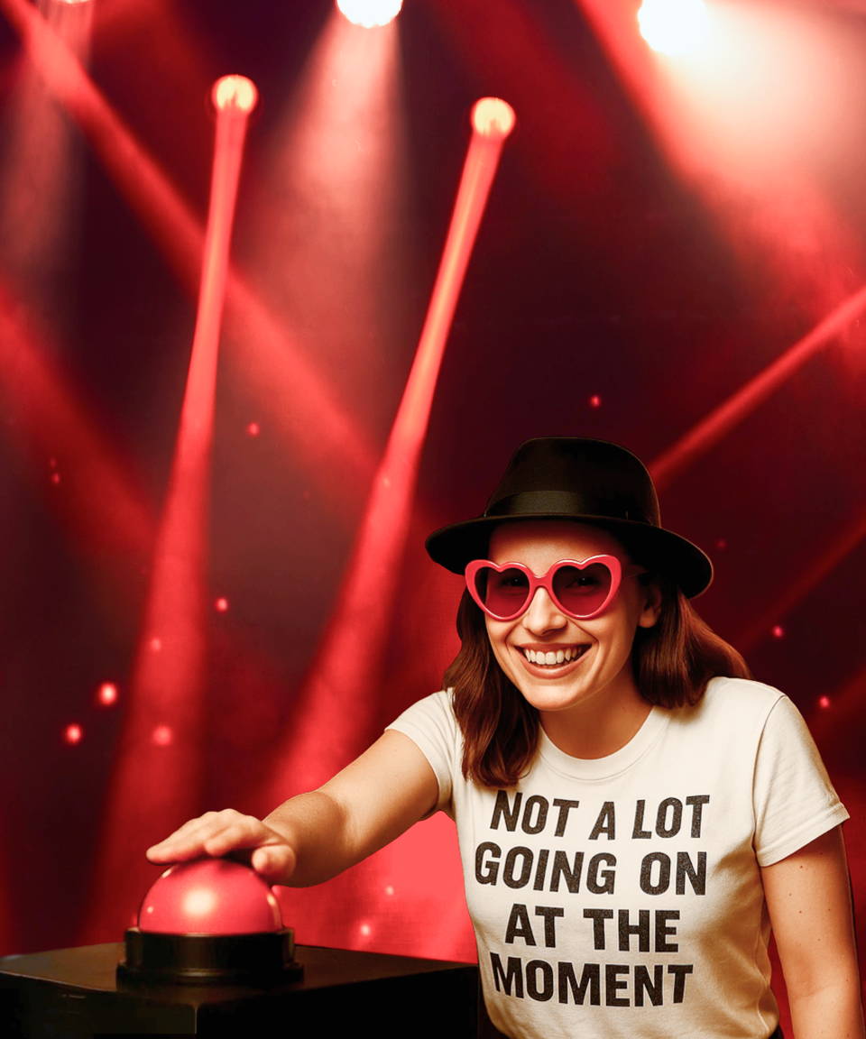 Woman with a swifty shirt, heart-shaped sunglasses & a black hat, with her hand hovering over a red buzzer 