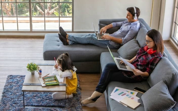 A mom & dad working from their couch in their home, while their kid colours on the floor
