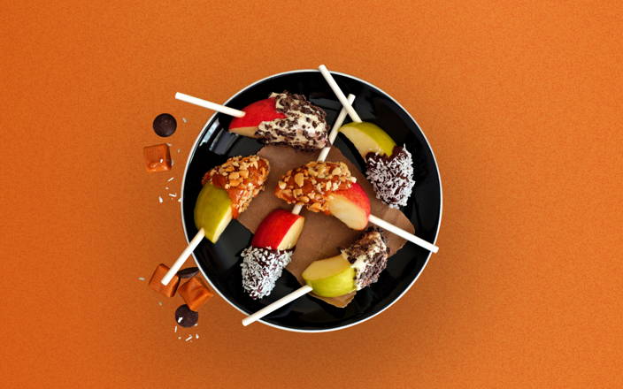A bowl of caramel and chocolate dipped apple slices on sticks for Confetti's Virtual Candy Apple Classes Online
