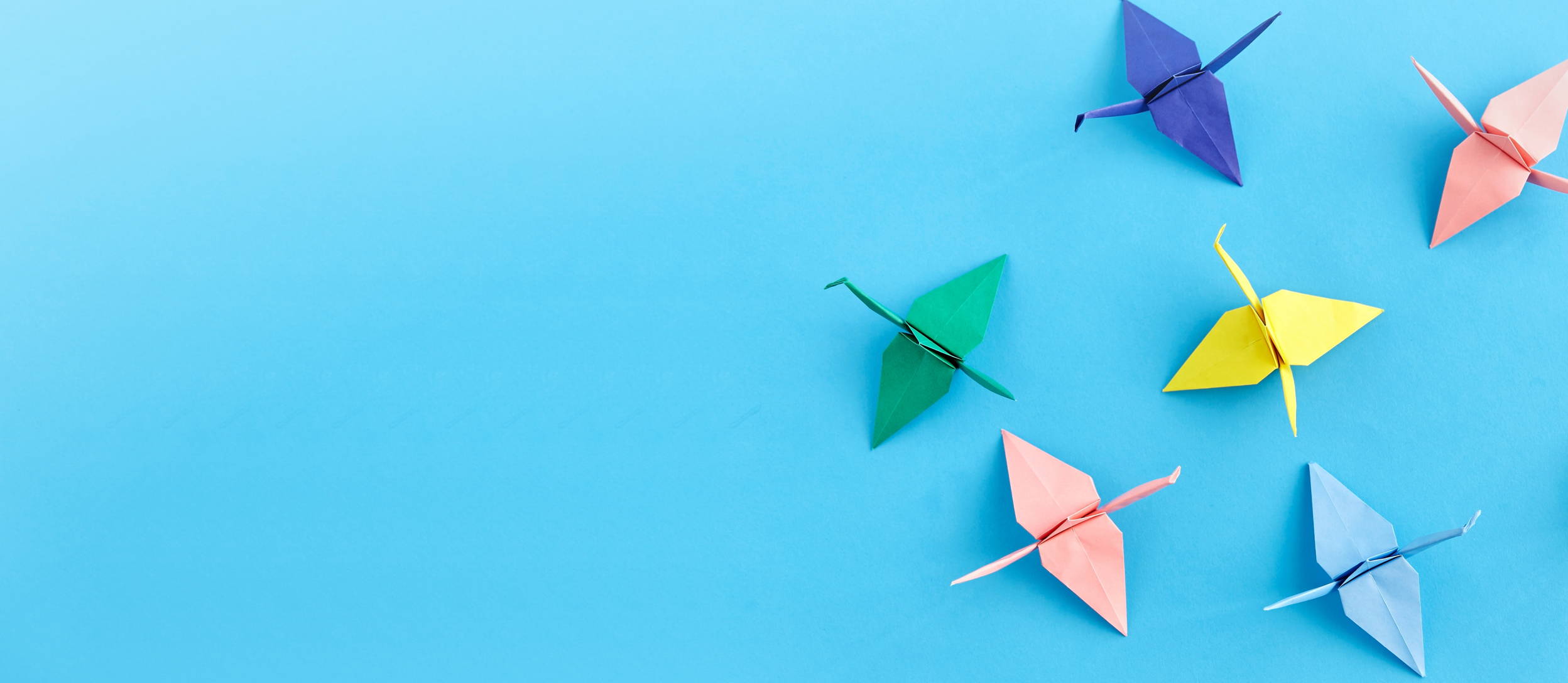 Multicolored folded origami crane designs against a blue background (large)