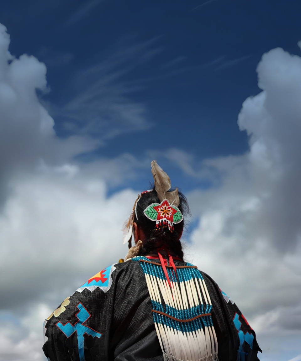 An indigenous person in traditional garments looking up at the clouds