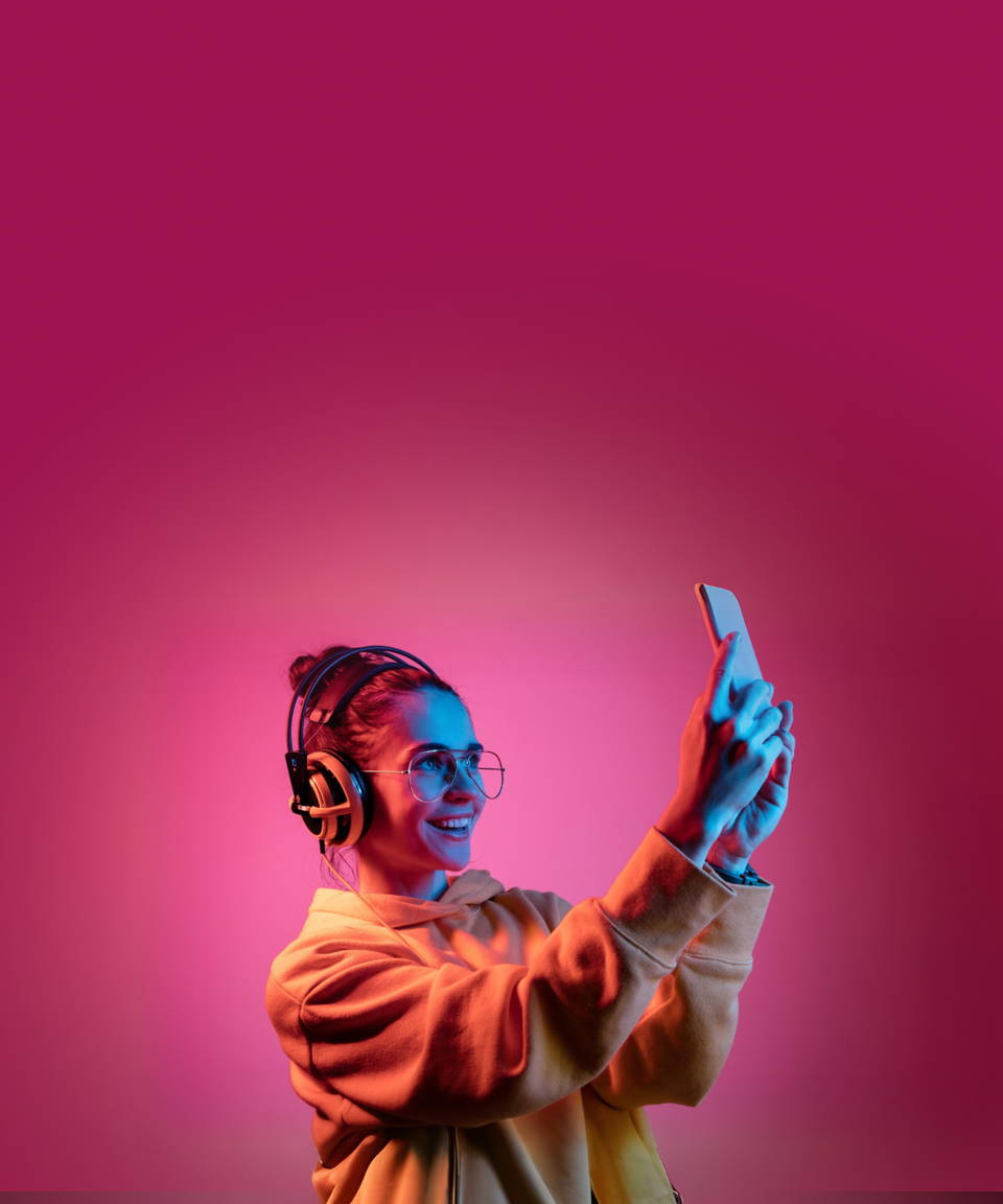 Smiling woman wearing headphones & an orange sweater, over a pink background, she's taking a photo