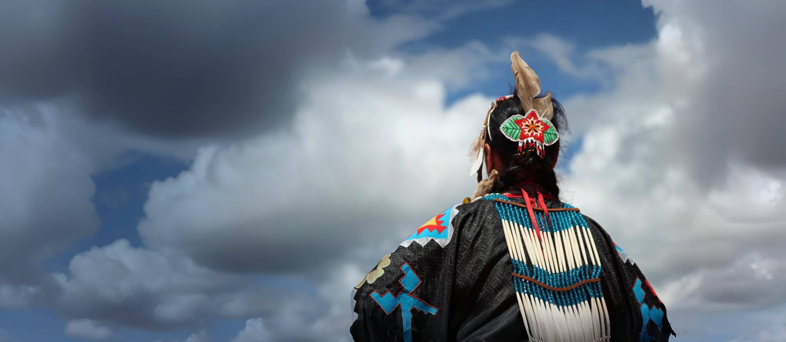 An indigenous person in traditional garments looking up at the clouds