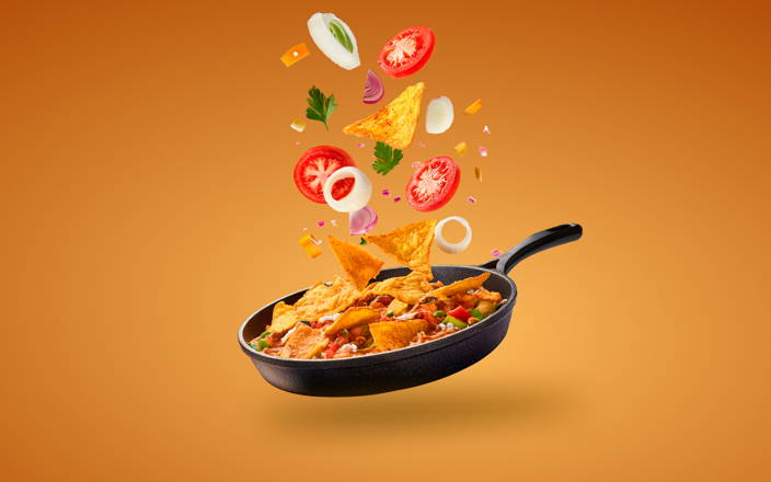 Chilaquiles cooking in a pan with vegetable garnishes floating on top (preview)