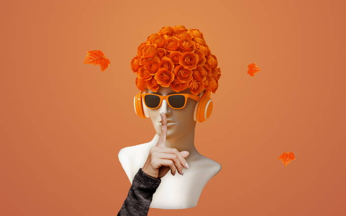 A statue head wearing orange headphones with autumnal flowers on its head with a finger in front of it's mouth in a 'silencing' gesture for Confetti's Virtual Team Building Taboo