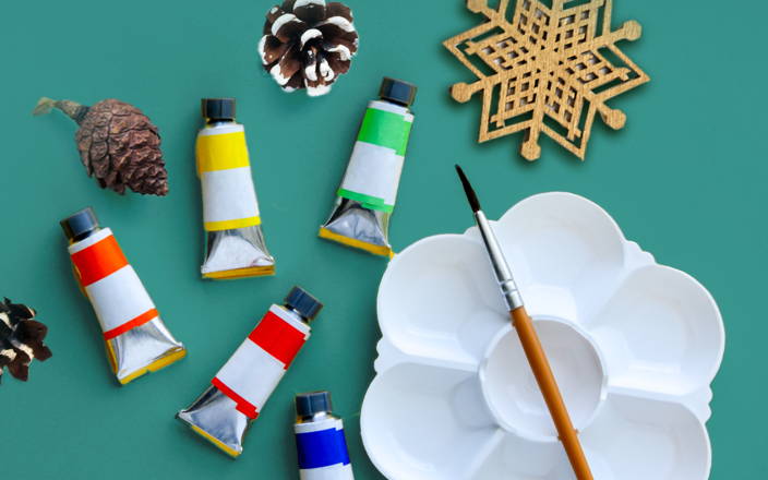 A snowflake, various paints, pinecones, an empty paint tray, and a paint brush for Confetti's Virtual Paint Night