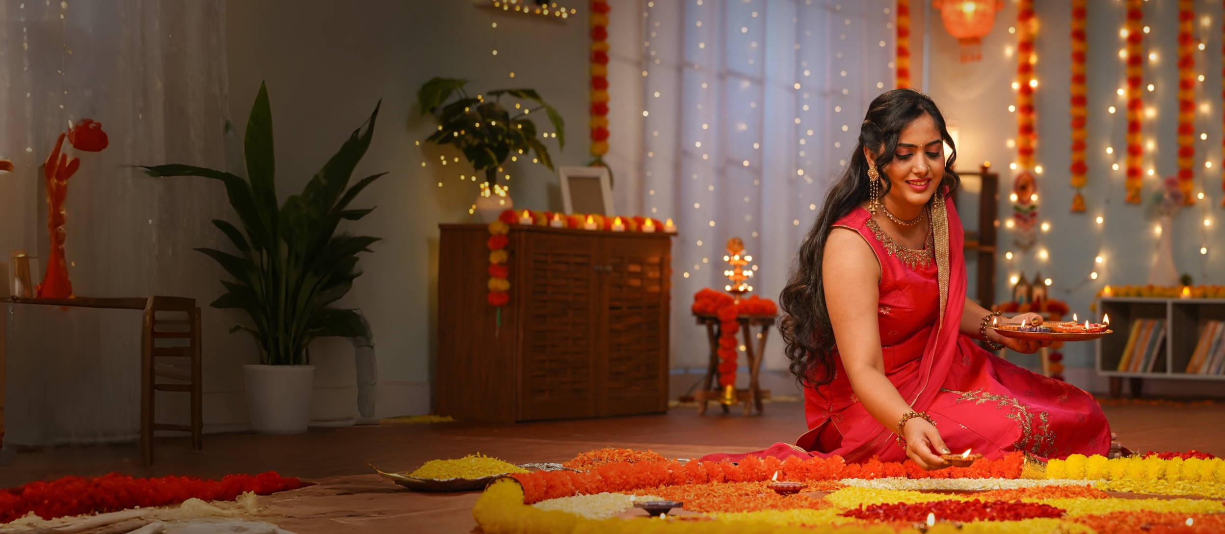 Indian woman sitting on the floor celebrating the holiday of Diwali, surrounded by bright colors, lights, and flowers.