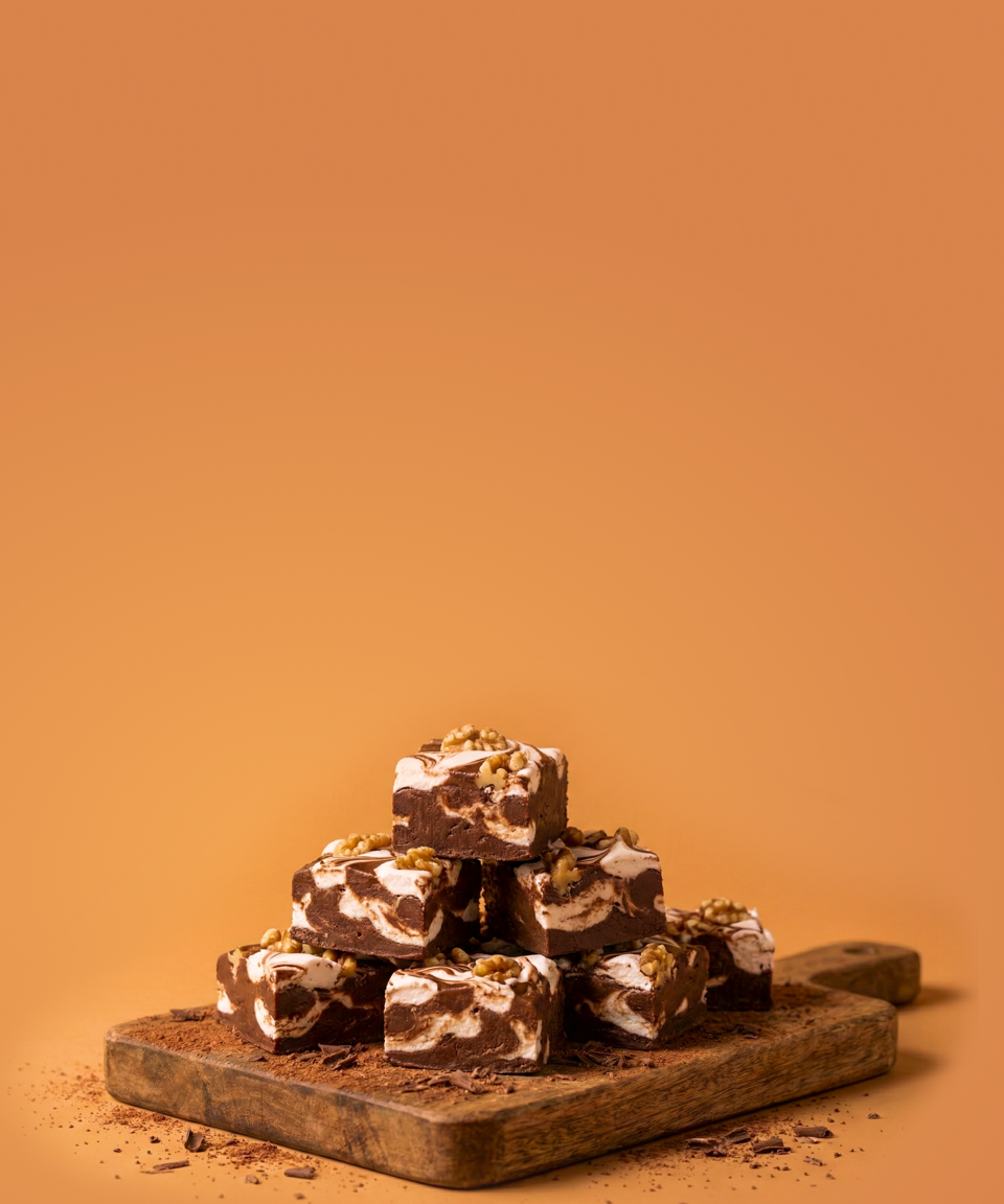 Pieces of fudge stacked on top of each other. Fudge has marshmallow swirls and walnuts.