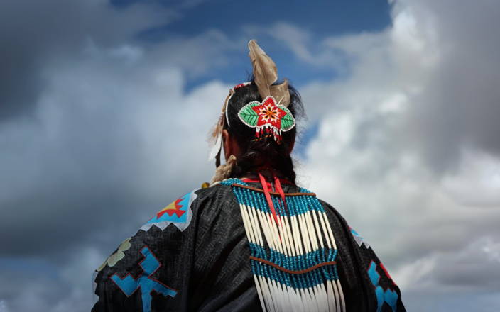 An indigenous person in traditional garments looking up at the clouds