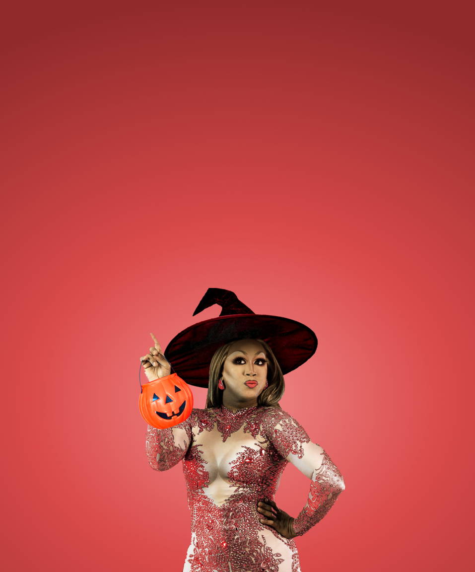 A drag queen wearing a witches hat and holding a jack-o-lantern bucket for Confetti's Virtual Halloween Drag Queen Trivia